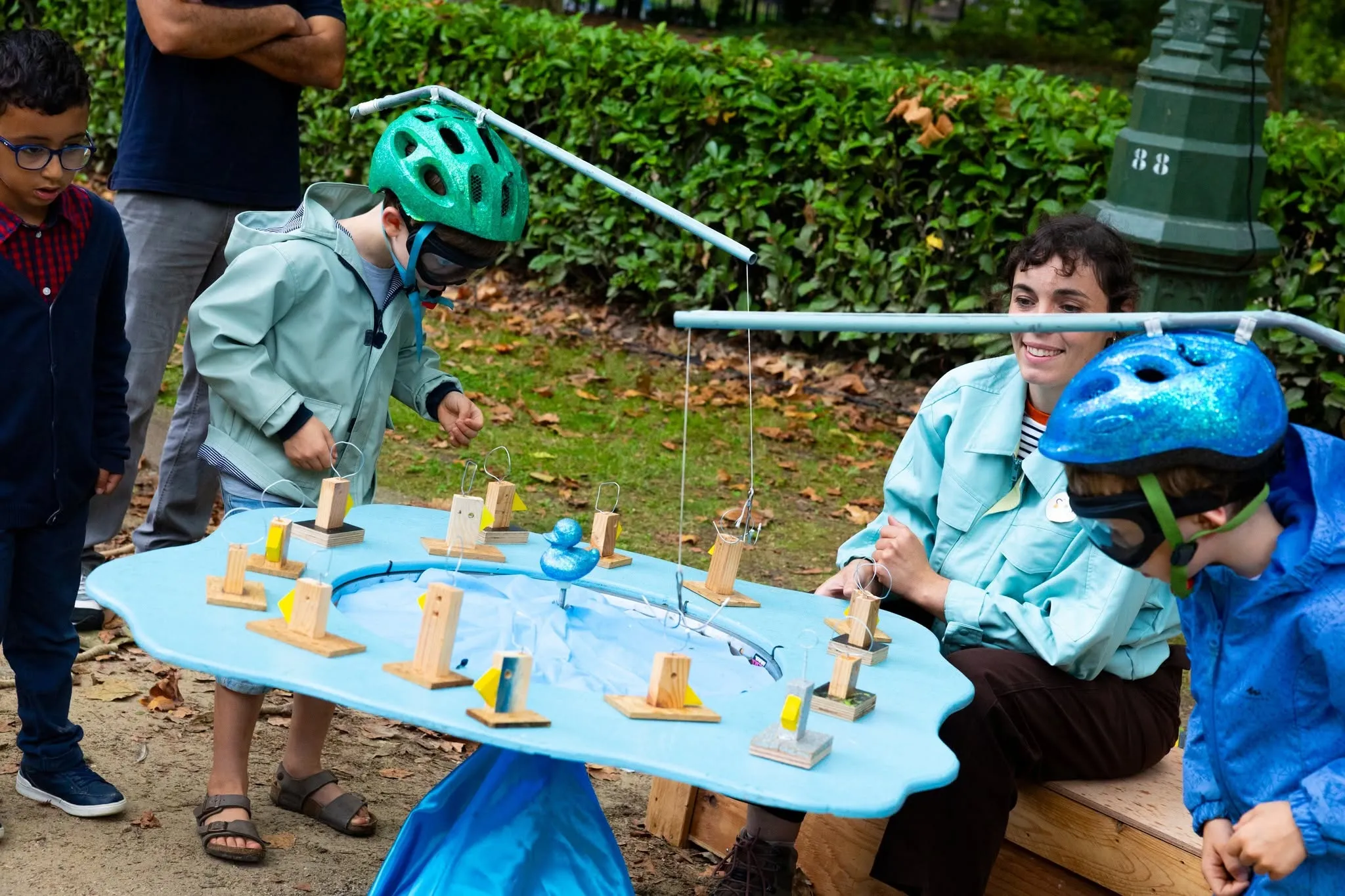 Kinderen met fietshelmen op spelen aan een blauwe watertafel met houten hengeltjes.