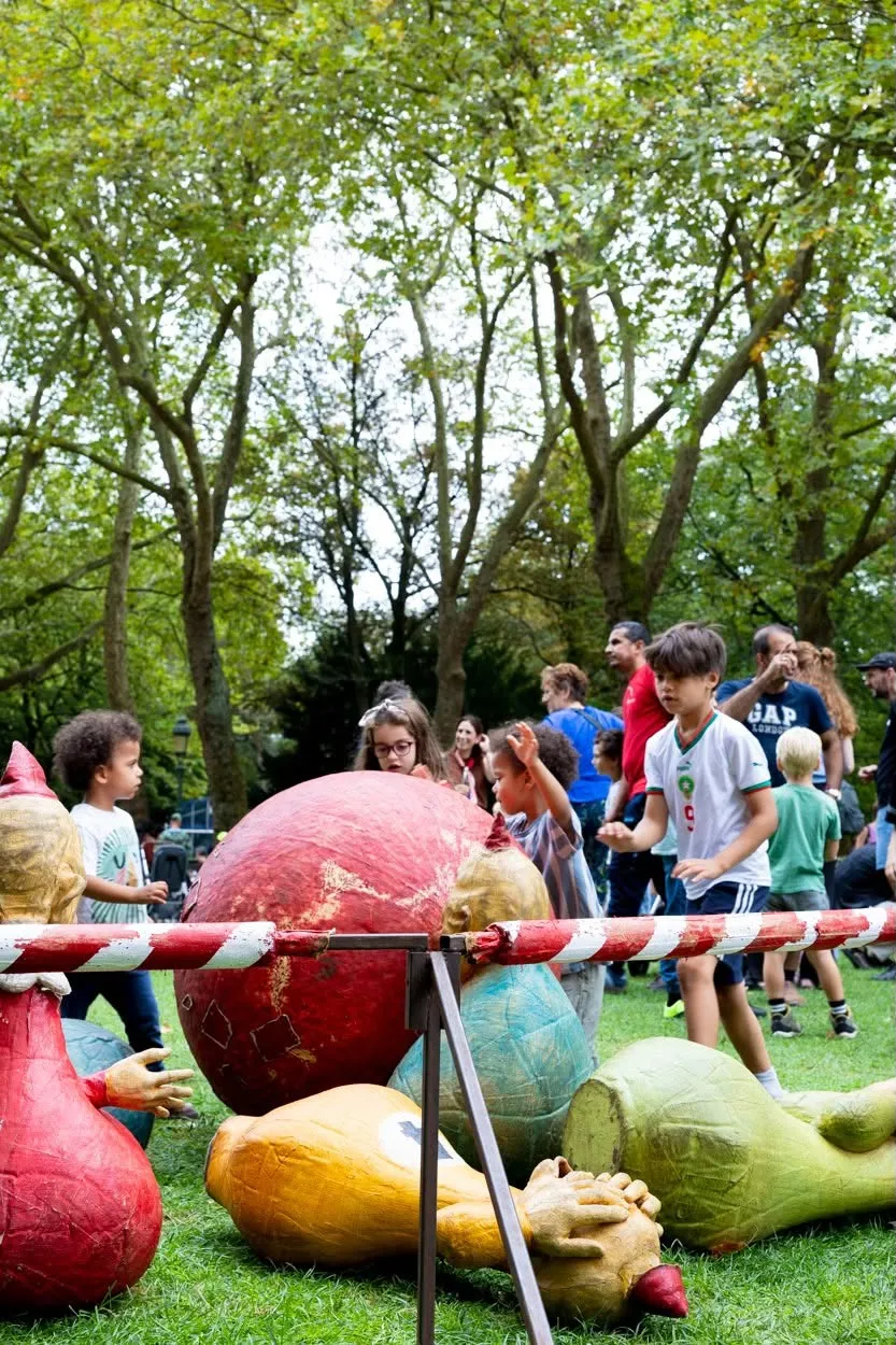 Reusachtige beschilderde fruitpoppen liggen in het gras, kinderen kijken nieuwsgierig toe.